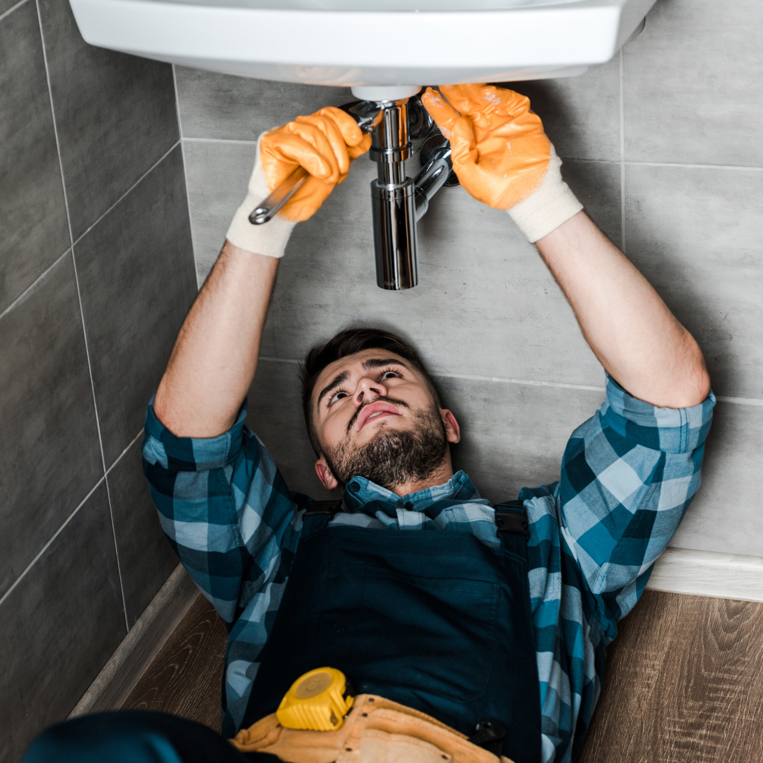 bearded repairman fixing water damage with adjustable wrench in bathroom Bärtiger Handwerker, der mit einem verstellbaren Schraubenschlüssel Wasserschäden im Badezimmer repariert.