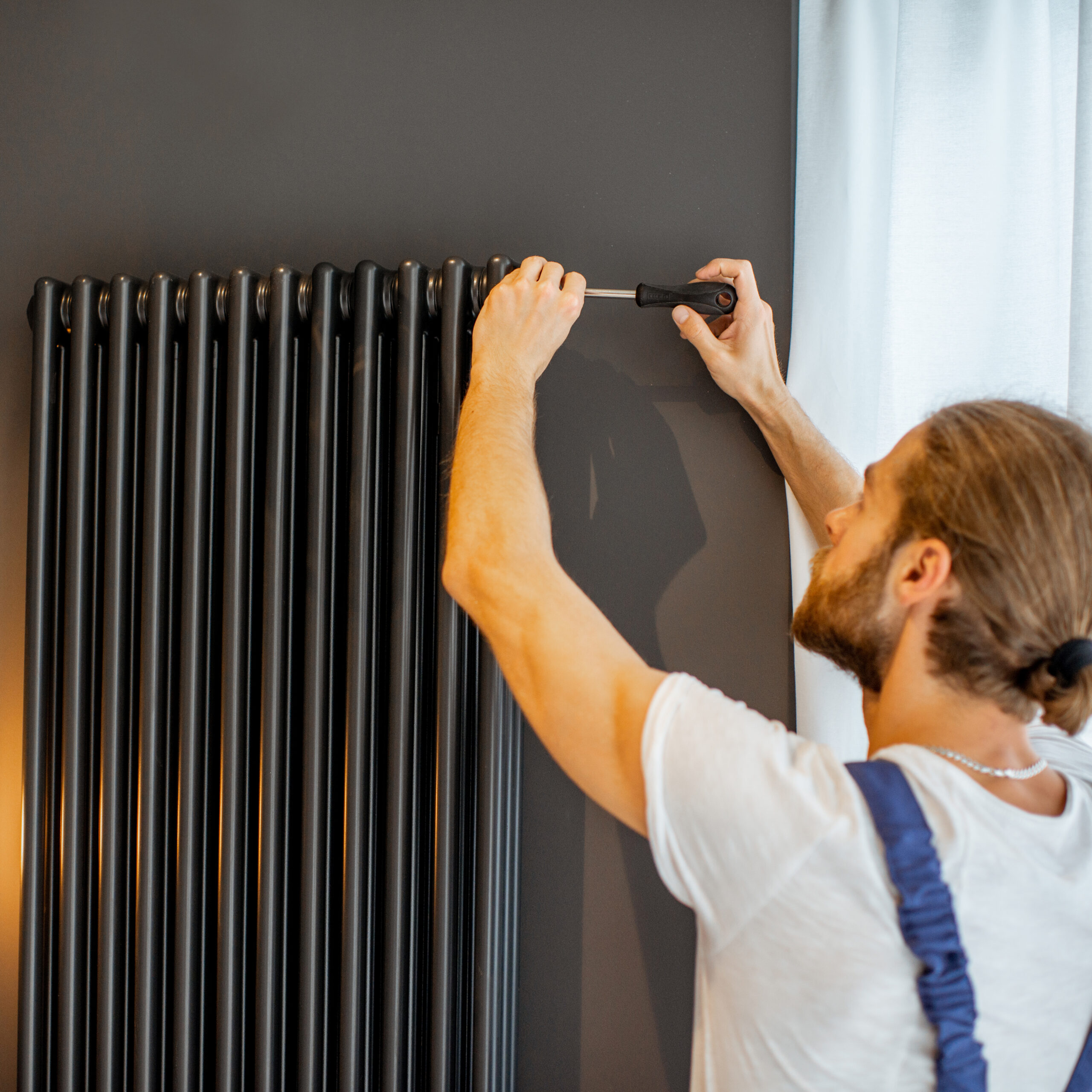 Handyman setting water radiator Handwerker lässt Luft aus dem Warmwasserheizkörper zu Hause ab.