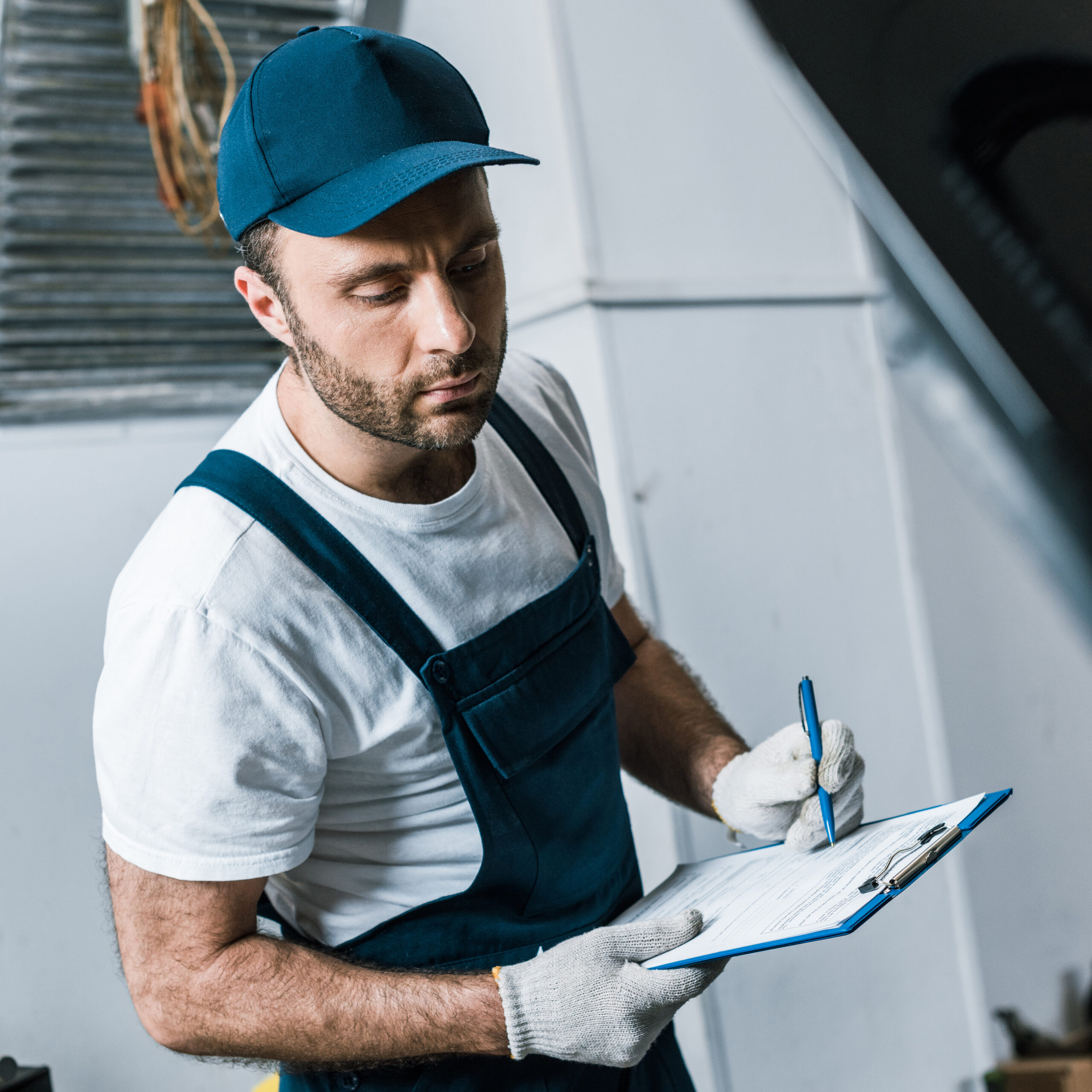 selective focus of handsome repairman in cap holding pen and clipboard